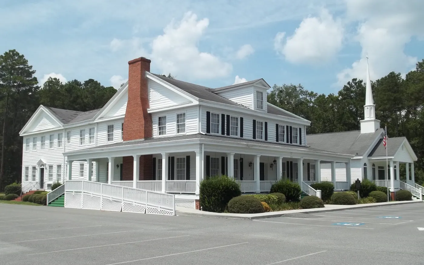 The historic Richmond Hill Community House, a white two-story building with a wraparound porch and a church steeple behind it